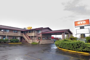Um motel de dois andares com telhado vermelho, uma escadaria visível e uma placa indicando OYO Hotel.