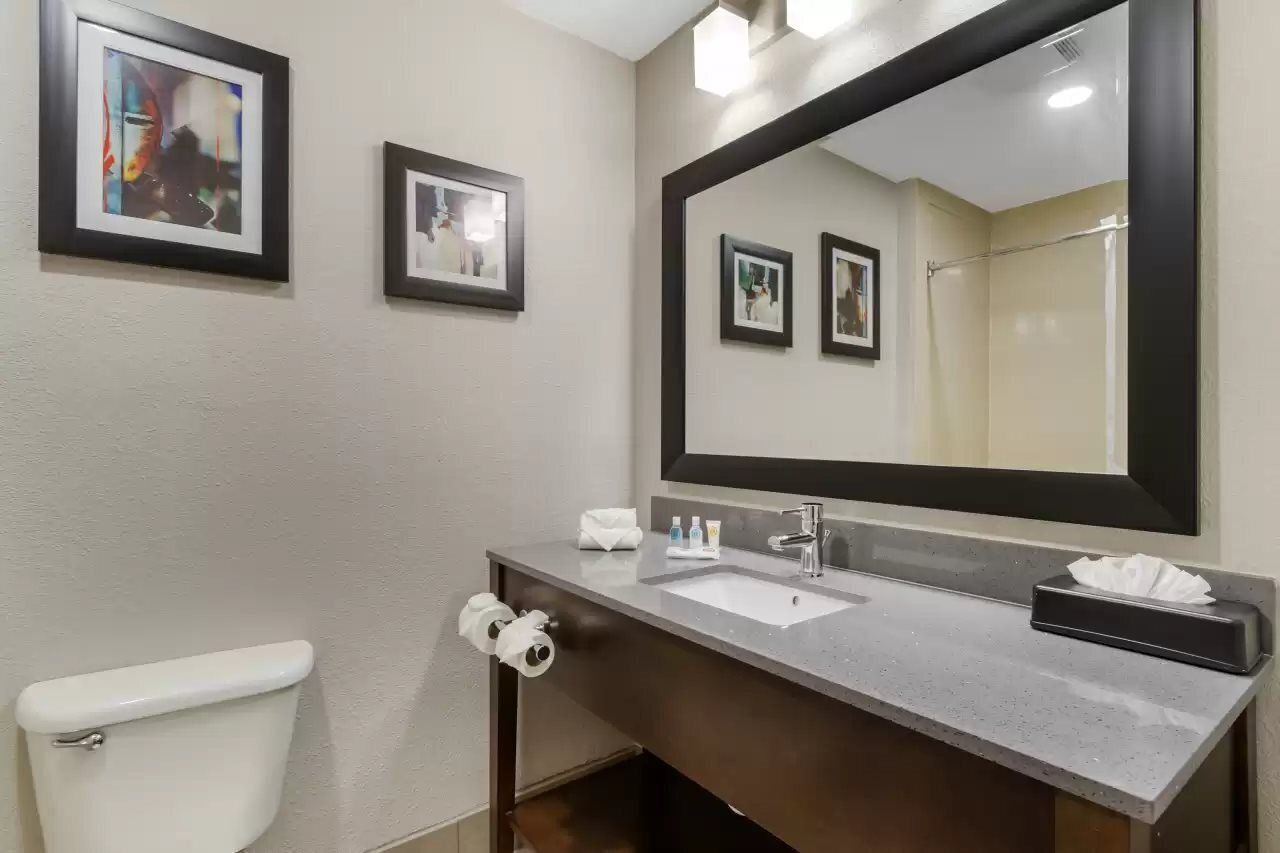 Une salle de bain avec des toilettes blanches, un lavabo avec un miroir et des tableaux encadrés accrochés au mur.