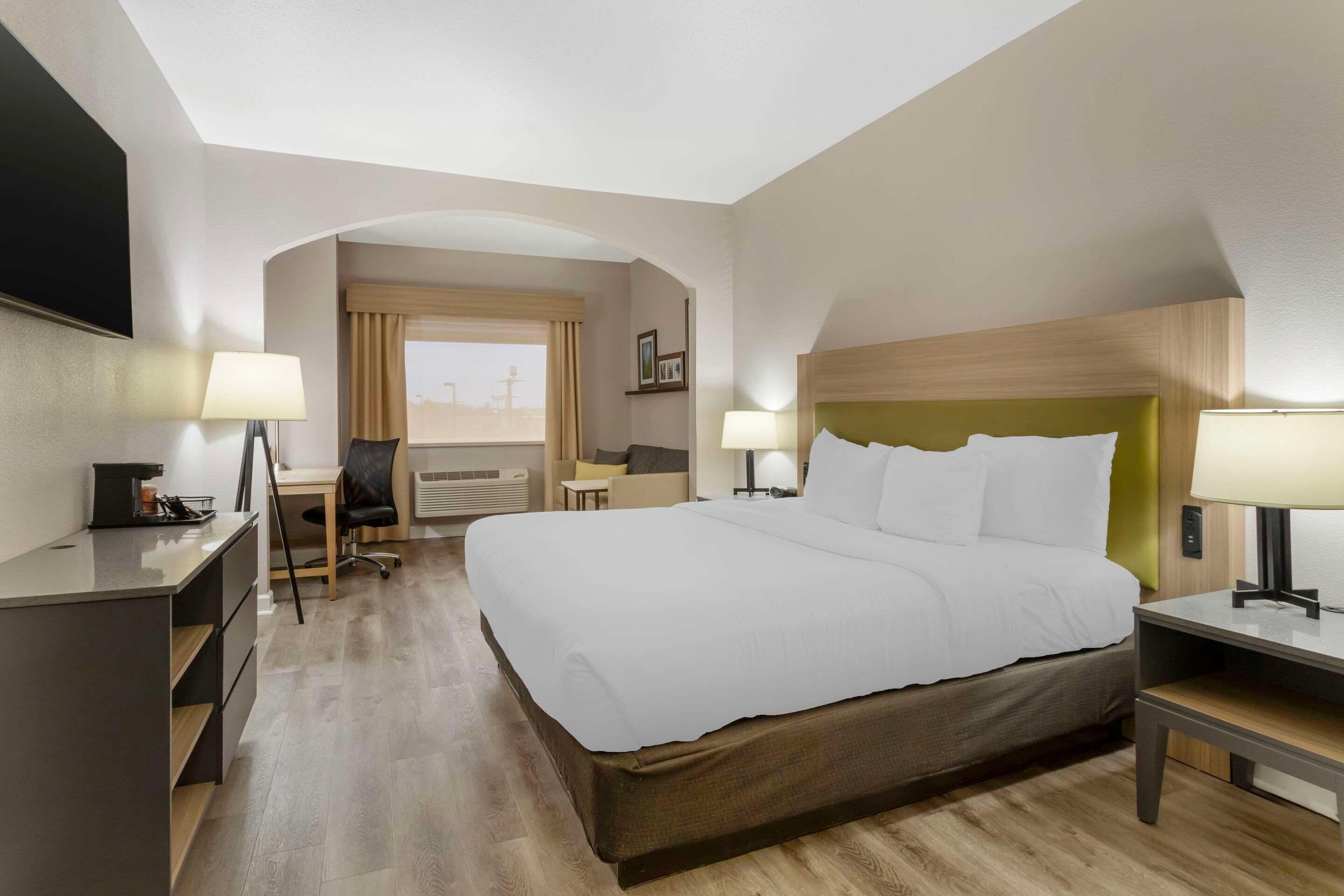 Ein Hotelzimmer mit einem großen Bett, einem Schreibtisch, einem Stuhl und einem Fenster mit Vorhängen.