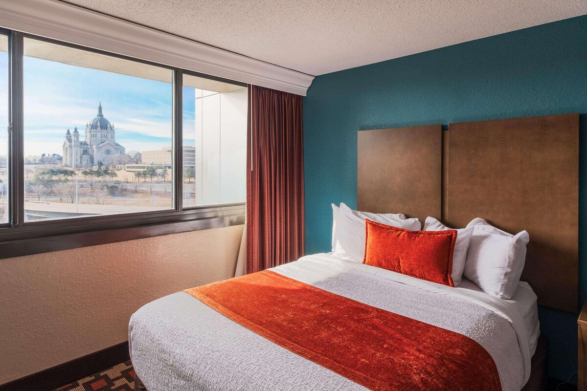 Une chambre d’hôtel avec un grand lit, une vue sur une cathédrale et un mur de couleur turquoise.