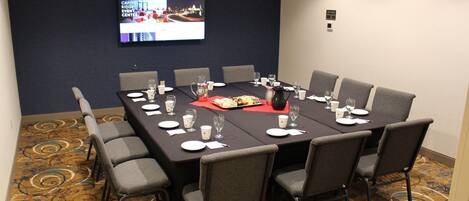 A conference room with a long table, chairs, a screen, and a carpeted floor.