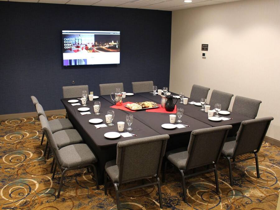 A conference room with a long table, chairs, a screen, and a carpeted floor.