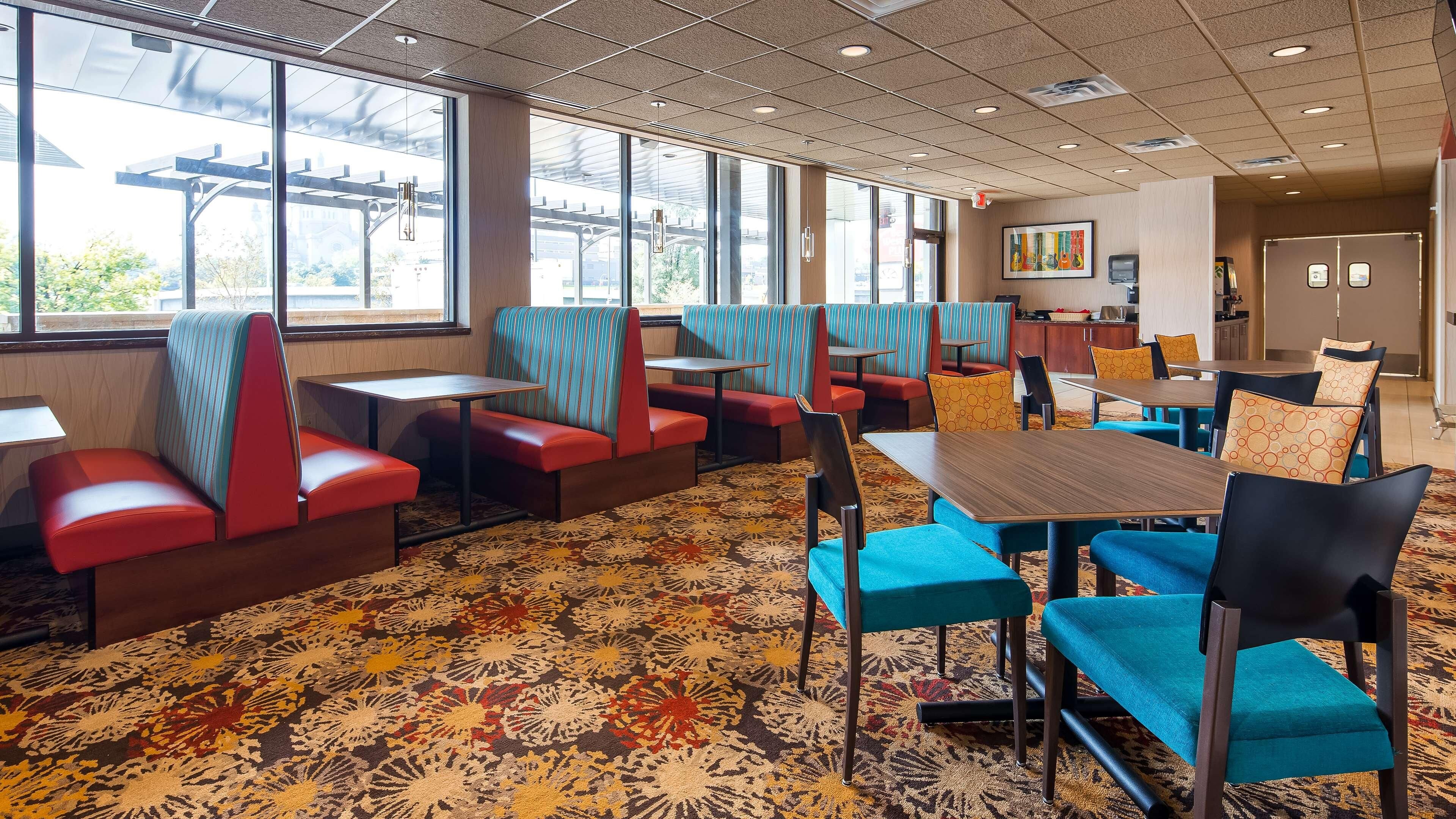 Un comedor de hotel con cabinas y mesas, ventanas amplias y una alfombra estampada.