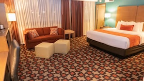 A hotel room with a bed, a sofa, two ottomans, a small table, and curtains. - Radisson Hotel St. Paul Downtown (St. Paul)