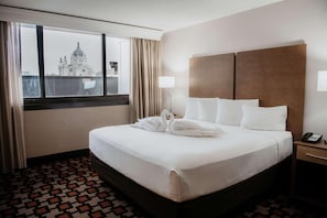 A hotel room with a large bed, a nightstand, a lamp, and a view of a building through the window. - Radisson Hotel St. Paul Downtown (St. Paul)
