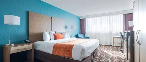 A hotel room with a bed, bedside tables, a desk, a chair, a wardrobe, and a window with curtains.