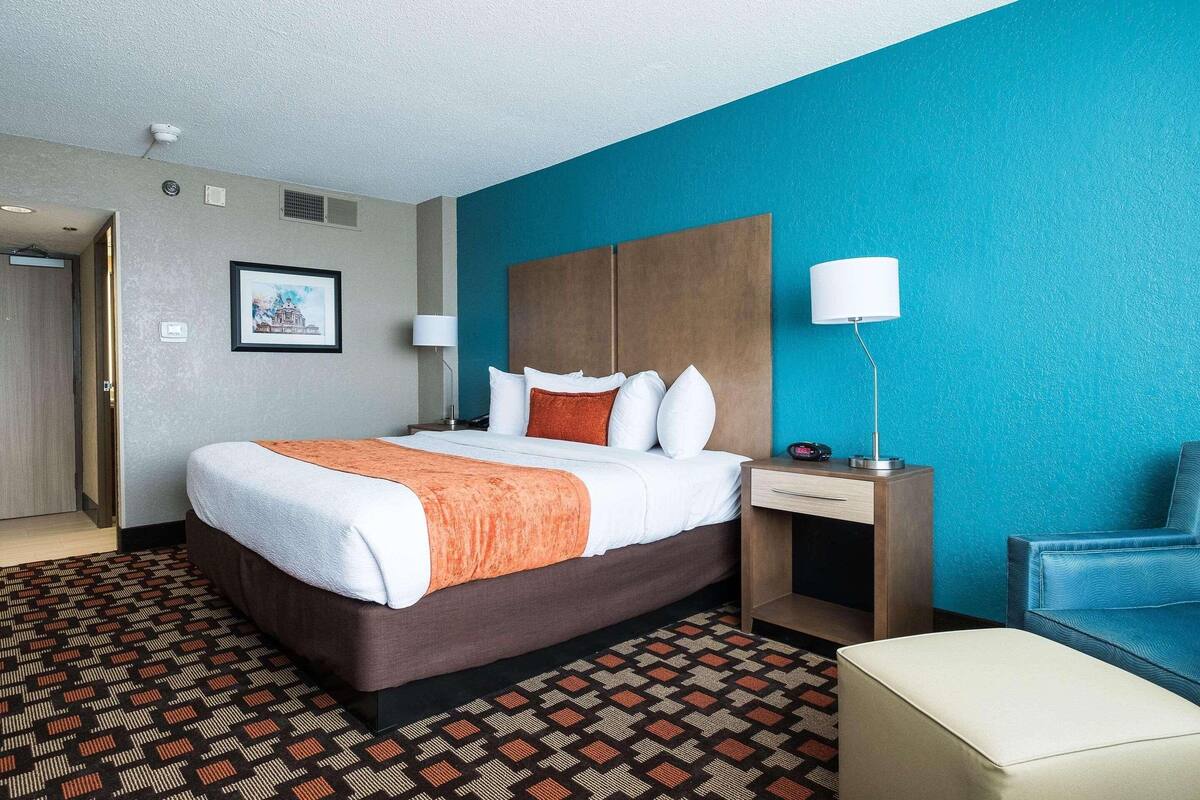 A hotel room with a bed, a desk, a chair, and a wall-mounted lamp.