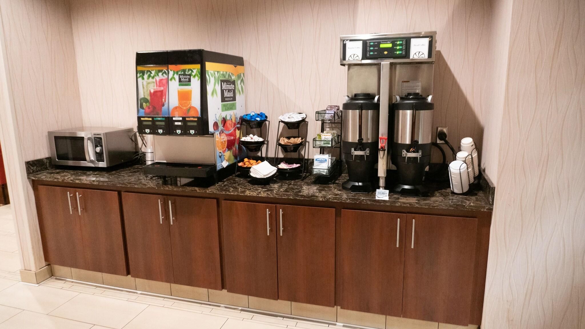 A kitchenette with a microwave, a juice dispenser, a coffee maker, and a blender.