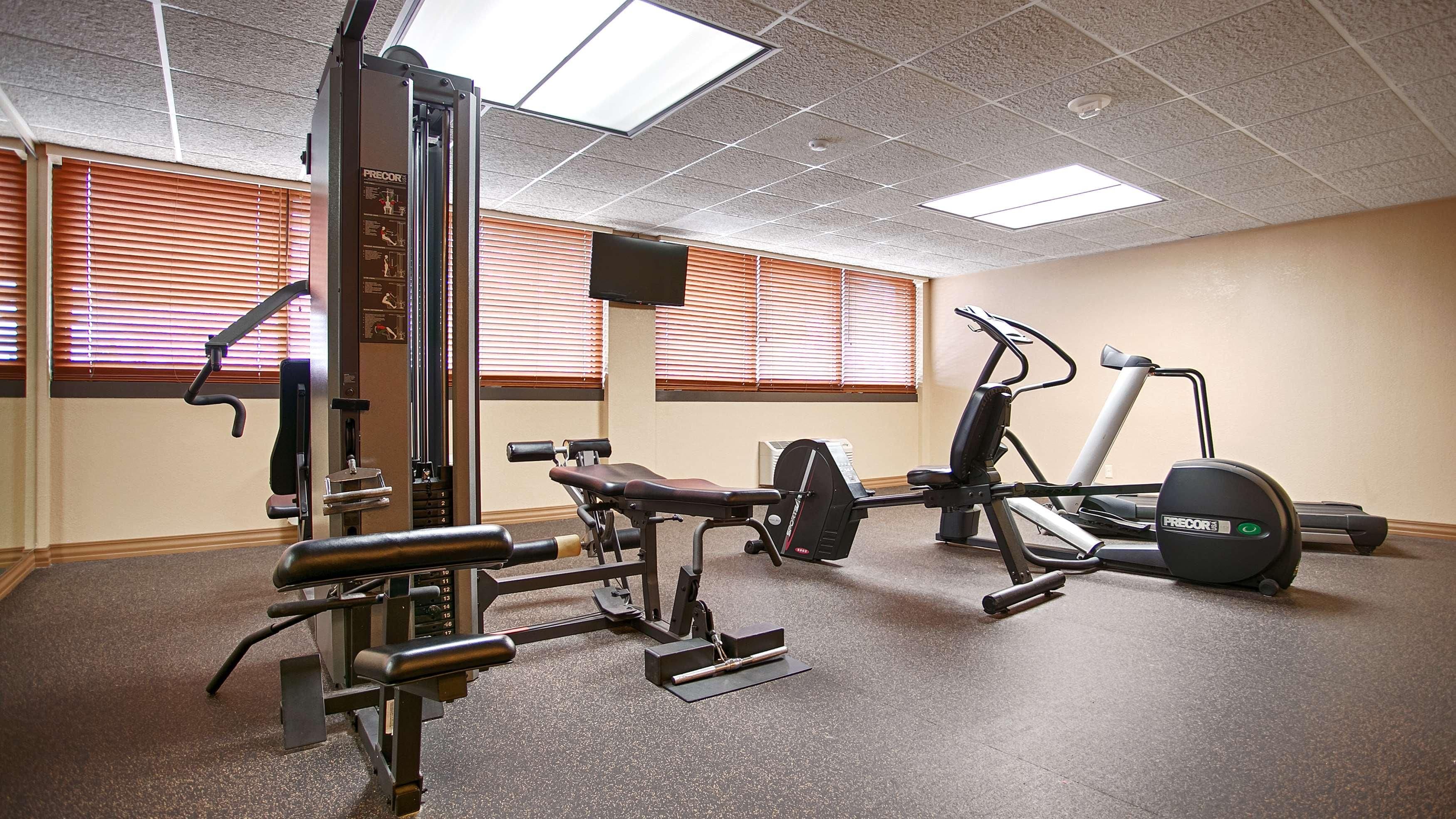 Uma academia com equipamentos de ginástica, incluindo um banco de supino, um aparelho de leg press e uma máquina elíptica.
