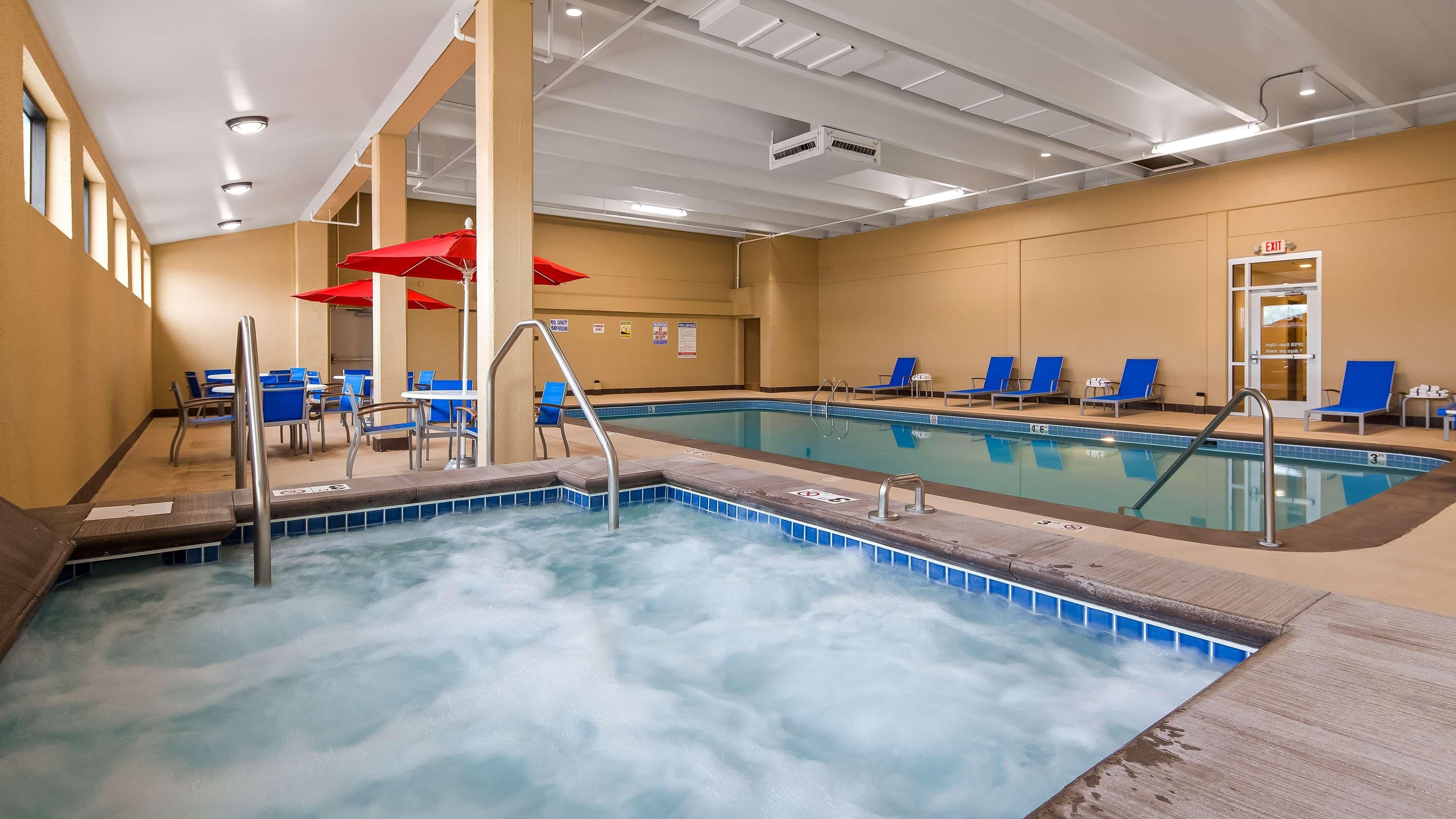 Una piscina con area idromassaggio, poltrone da relax blu e ombrelloni rossi.