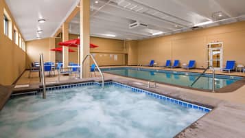 Una piscina con area idromassaggio, poltrone da relax blu e ombrelloni rossi.
