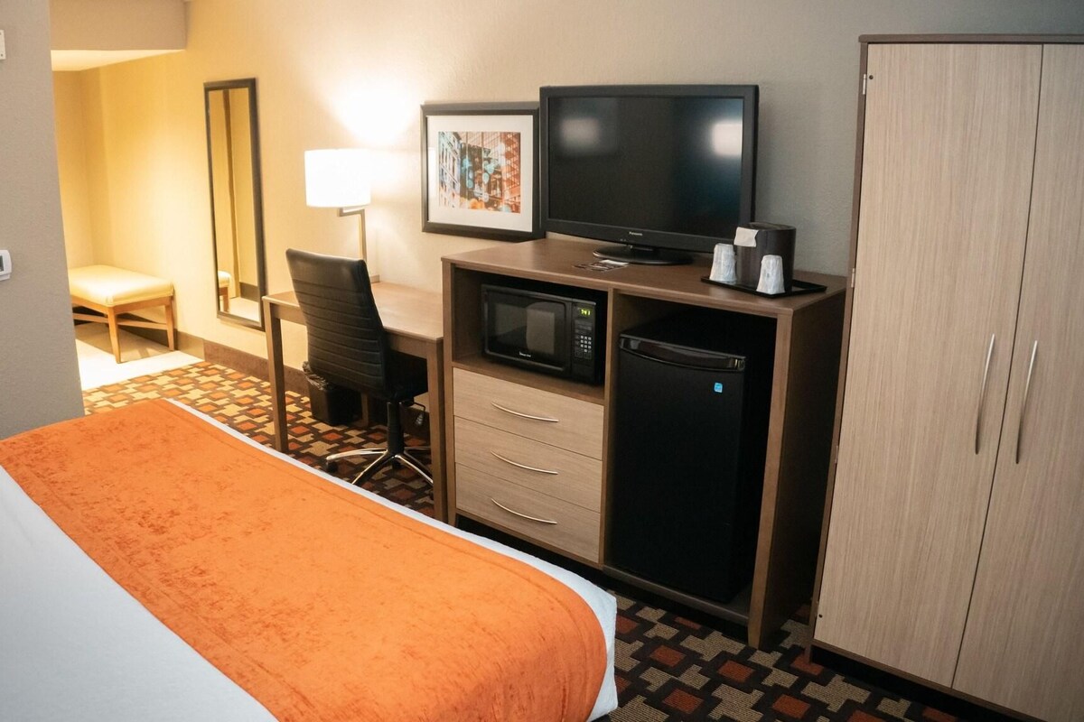 Une chambre d’hôtel équipée d’un lit, d’un bureau avec un ordinateur, d’une télévision, d’un four à micro-ondes et d’une armoire.
