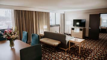 A hotel room with a sofa, a small table, a TV, and a desk with a lamp.