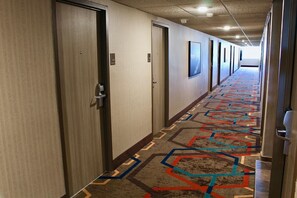 Un pasillo de hotel con pisos alfombrados, puertas y un techo con iluminación empotrada.