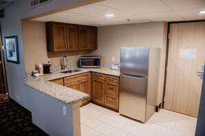 A compact kitchen with wooden cabinets, a stainless steel refrigerator, a microwave, and a sink. - Radisson Hotel St. Paul Downtown (St. Paul)