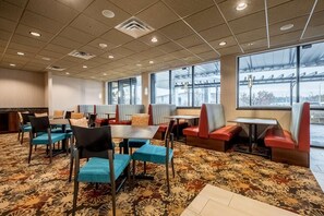 Un comedor de hotel con mesas y cabinas, alfombra estampada y ventanas amplias.