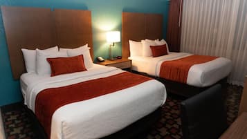A hotel room with two beds, a nightstand with a lamp, and a patterned carpet.