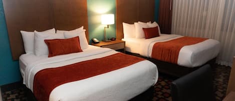 A hotel room with two beds, a nightstand with a lamp, and a patterned carpet.