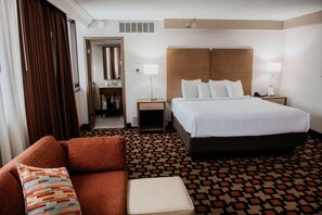 Una habitación de hotel con una cama grande, un sofá, una mesita y un espejo.