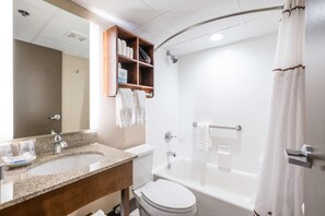 A bathroom with a sink, toilet, bathtub, shower curtain, and a mirror with a shelf above it. - Radisson Hotel St. Paul Downtown (St. Paul)