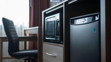Een kleine keuken met een magnetron, een koelkast en een stoel.