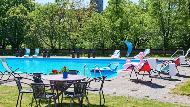 Una piscina con lettini, un tavolo e sedie, e una torre d'acqua sullo sfondo.