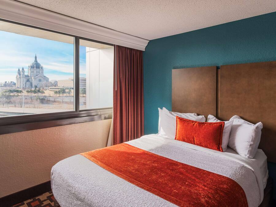 Une chambre d’hôtel avec un grand lit, une vue sur une cathédrale et un mur d’accent de couleur turquoise.