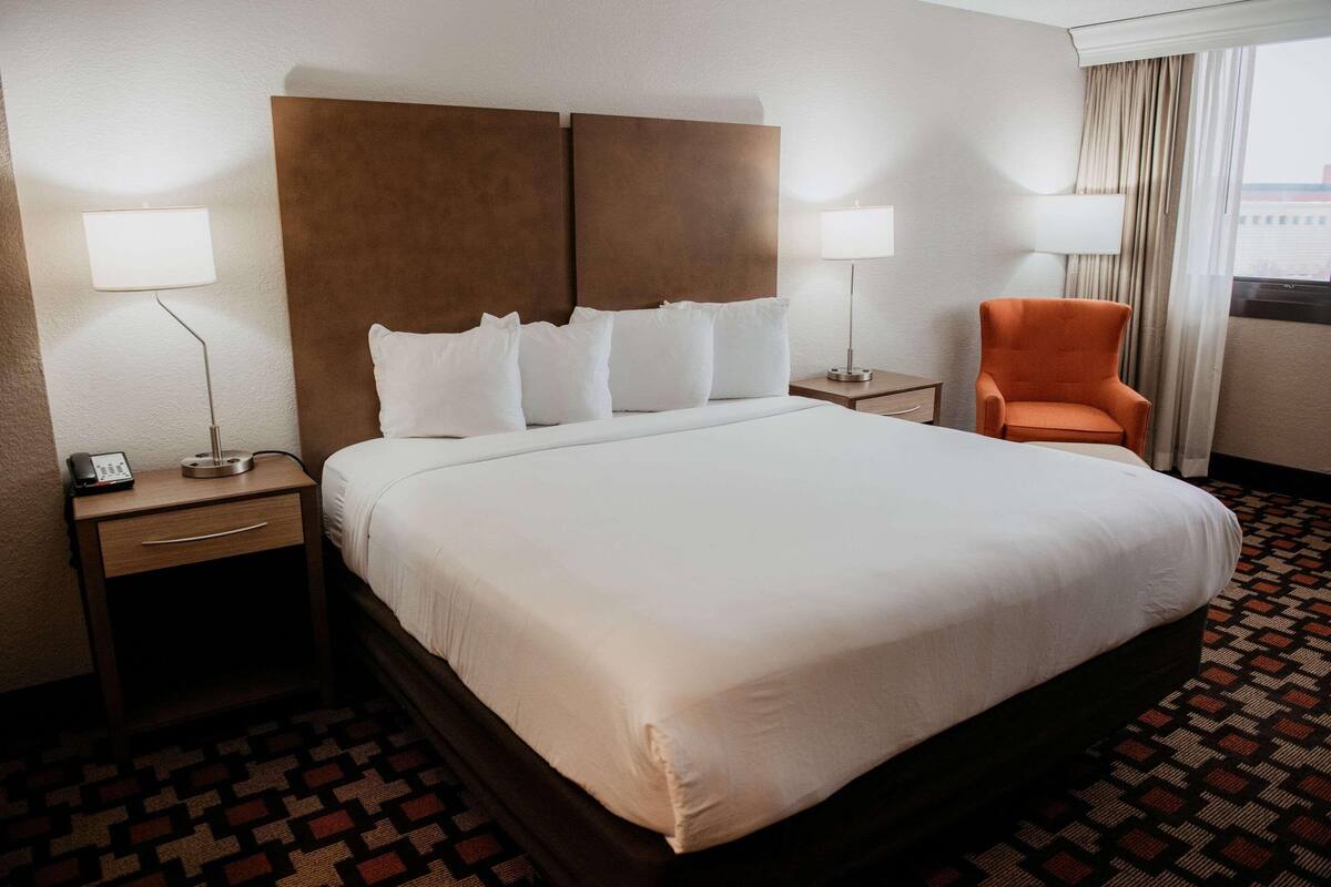 A hotel room with a large bed, two bedside tables, a chair, and a window with curtains.