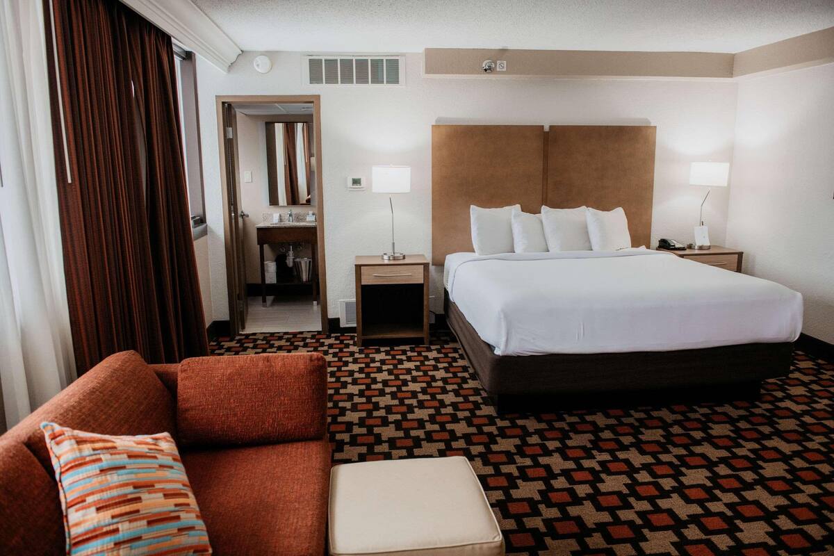 A hotel room with a large bed, a sofa, a small table, and a mirror.