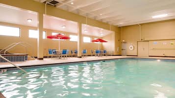 An indoor swimming pool with clear water, blue chairs, and red umbrellas.
