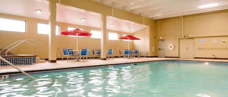 An indoor swimming pool with clear water, blue chairs, and red umbrellas.