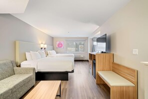 A hotel room with a bed, a sofa, a desk, a bench, a TV, and a window with a view. - Best Western Lake Oswego Portland Hotel Suites (Lake Oswego)