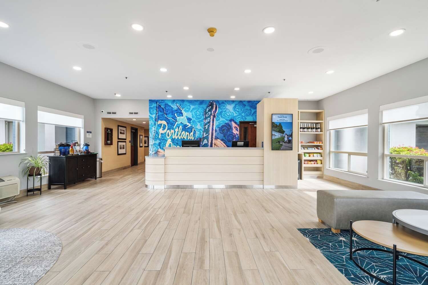 A hotel lobby with a reception desk, a large blue mural, a seating area, and a bookshelf.