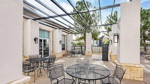 An outdoor patio area with round tables and chairs, a pergola structure, and stone walls. - Best Western Lubbock West Inn and Suites (Lubbock)