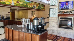 A hotel lobby with a coffee station, a fireplace, a television, and a mural on the wall. - Best Western Lubbock West Inn and Suites (Lubbock)