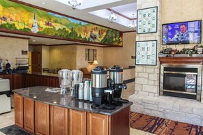 A hotel lobby with a coffee station, a fireplace, a television, and a mural on the wall. - Best Western Lubbock West Inn and Suites (Lubbock)