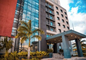 A modern hotel with a glass facade, a covered entrance, and a palm tree in the foreground. - Crowne Plaza Dar Es Salaam (Dar es Salaam)