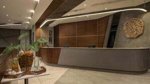A modern reception area with a curved reception desk, a decorative wall piece, and a plant arrangement on the left. - Crowne Plaza Dar Es Salaam (Dar es Salaam)