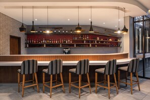 A bar area with wooden bar stools, a counter, and overhead pendant lighting. - Crowne Plaza Dar Es Salaam (Dar es Salaam)