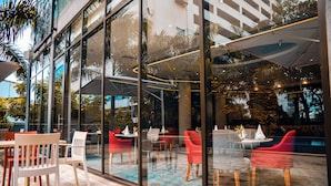 An outdoor seating area with tables and chairs, a pool, and a glass wall reflecting the surroundings. - Crowne Plaza Dar Es Salaam (Dar es Salaam)