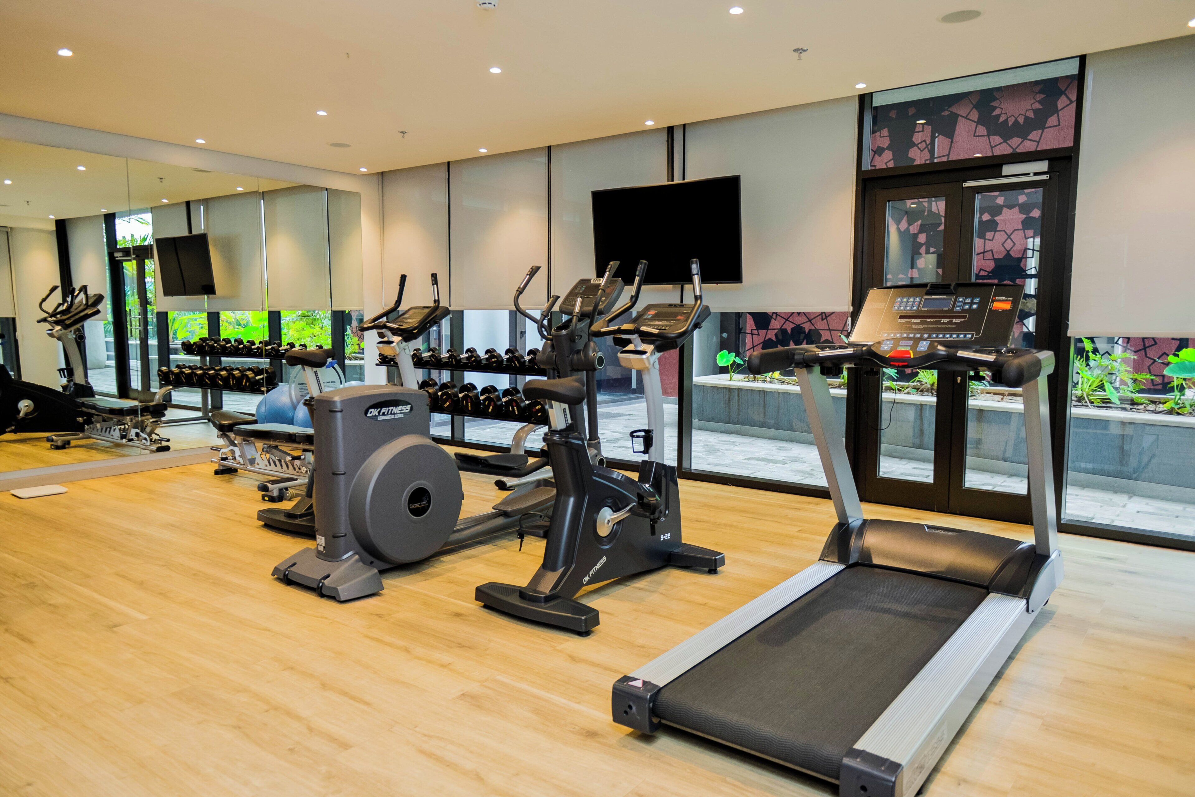 A modern gym with treadmills, elliptical machines, and weight stations.