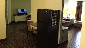Habitación de hotel compacta con kitchenette, televisión, pequeña mesa de comedor y una silla.
