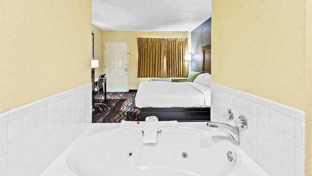 Een hotelkamer met een groot wit bad, een bed met witte lakens, een deur en een gordijn.
