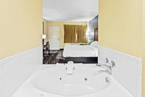 Ein Hotelzimmer mit einer großen, weißen Badewanne, einem Bett mit weißer Bettwäsche, einer Tür und einem Vorhang.