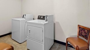 Een wasserette met twee witte wasmachines en een stoel.