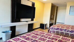 Een hotelkamer met een flatscreen televisie aan de muur, een bed met een bloemenprint dekbed en een kleine prullenbak.