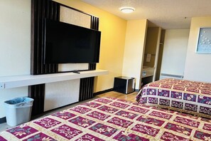 A hotel room with a flat-screen TV mounted on a wall, a bed with a floral-patterned bedspread, and a small trash bin. - King City Motel by OYO Pasco (Pasco)