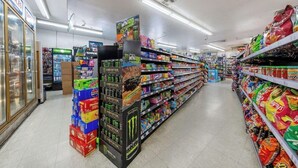 A grocery store aisle with shelves stocked with snacks and beverages, a refrigerated section on the left, and a promotional display for Monster energy drinks. - King City Motel by OYO Pasco (Pasco)