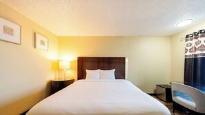 Een hotelkamer met een groot bed, een nachtkastje met een lamp, een bureau en een stoel.