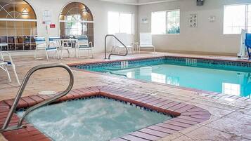 An indoor swimming pool with a hot tub, lounge chairs, and a sunlit room with arched windows.